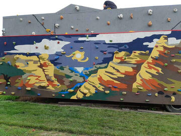 Impressionist mural of a canyon with river, painted on a rock-climbing wall.